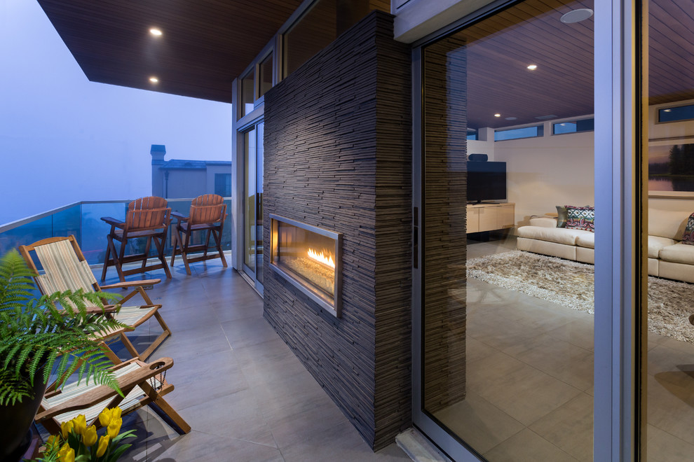 Inspiration for a small modern balcony in Los Angeles with with fireplace, a roof extension and glass railing.