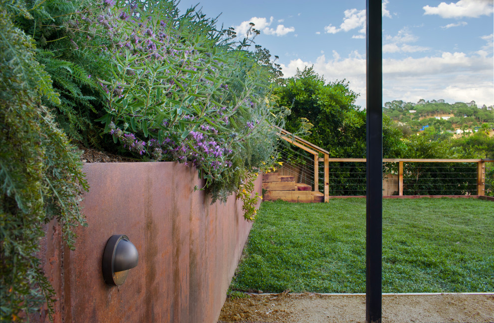 Ispirazione per un giardino xeriscape industriale esposto in pieno sole di medie dimensioni e dietro casa in primavera con graniglia di granito, recinzione in legno e un muro di contenimento
