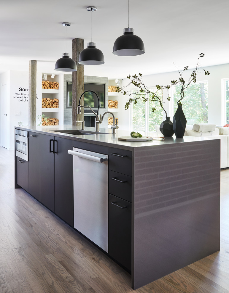 Design ideas for a large industrial galley eat-in kitchen in New York with an undermount sink, flat-panel cabinets, dark wood cabinets, grey splashback, black appliances, light hardwood floors, with island, beige floor and grey benchtop.