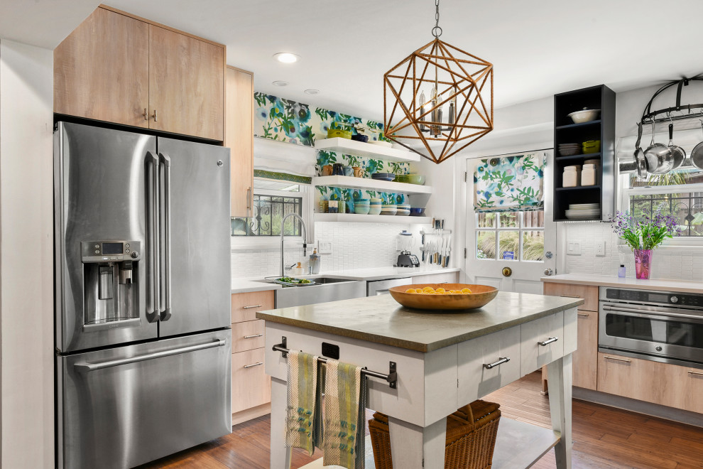 Mid-sized eclectic l-shaped kitchen in Jacksonville with a farmhouse sink, flat-panel cabinets, light wood cabinets, white splashback, medium hardwood floors, with island, brown floor and white benchtop.