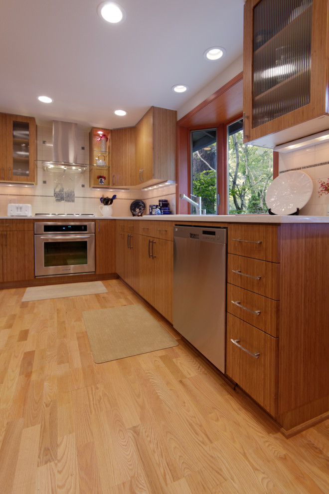 Mid-sized asian u-shaped eat-in kitchen in Portland with a drop-in sink, flat-panel cabinets, medium wood cabinets, quartz benchtops, white splashback, subway tile splashback, stainless steel appliances, light hardwood floors and no island.