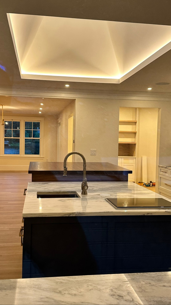 Large transitional u-shaped light wood floor, yellow floor and tray ceiling eat-in kitchen photo in Boston with an undermount sink, shaker cabinets, white cabinets, marble countertops, white backsplash, marble backsplash, paneled appliances, two islands and white countertops