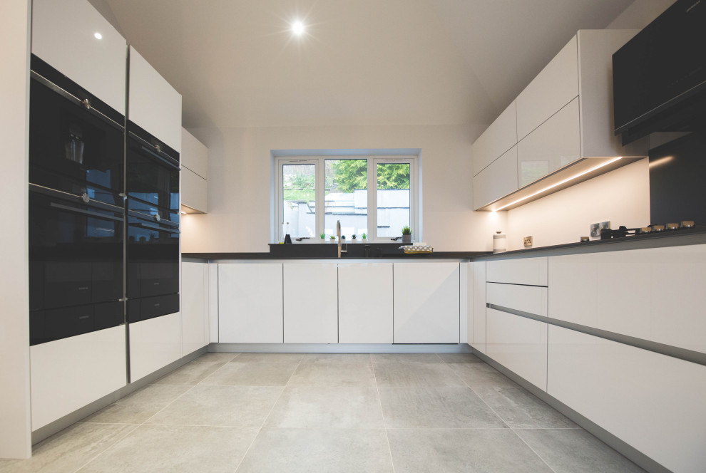 Large contemporary u-shaped kitchen/diner in Devon with an integrated sink, flat-panel cabinets, yellow cabinets, quartz worktops, black appliances, an island, grey floors, grey worktops and a feature wall.