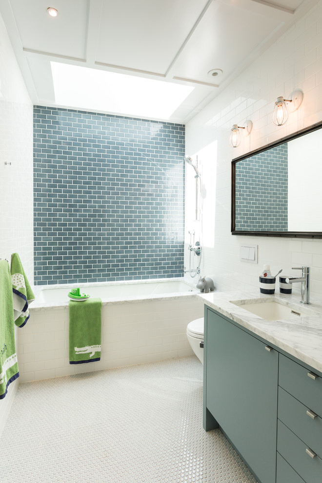 Photo of a contemporary kids bathroom in New York with flat-panel cabinets, blue cabinets, an alcove tub, a shower/bathtub combo, white tile, white walls, ceramic floors, an undermount sink, marble benchtops, white floor, a wall-mount toilet, subway tile and an open shower.