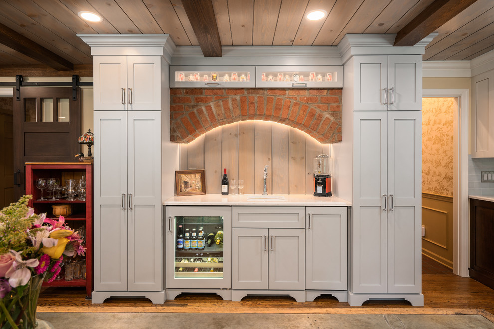 Example of a mid-sized transitional galley medium tone wood floor and brown floor eat-in kitchen design in Columbus with a farmhouse sink, shaker cabinets, dark wood cabinets, quartz countertops, white backsplash, subway tile backsplash, stainless steel appliances, an island and white countertops