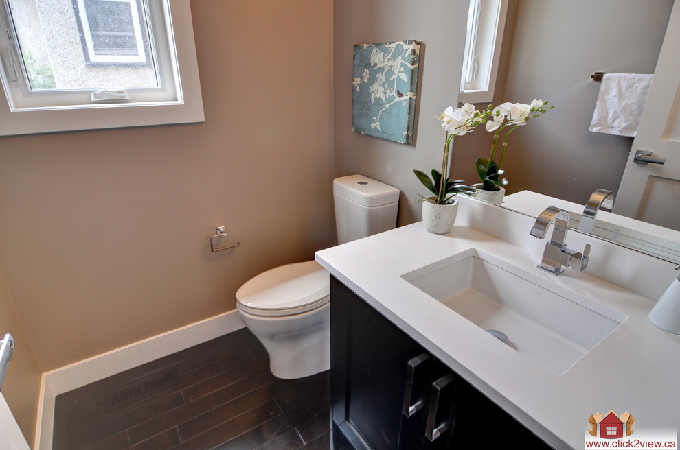 Design ideas for a mid-sized contemporary 3/4 bathroom in Calgary with an integrated sink, furniture-like cabinets, dark wood cabinets, solid surface benchtops, an alcove tub, an alcove shower, a two-piece toilet, white tile, ceramic tile, beige walls and dark hardwood floors.