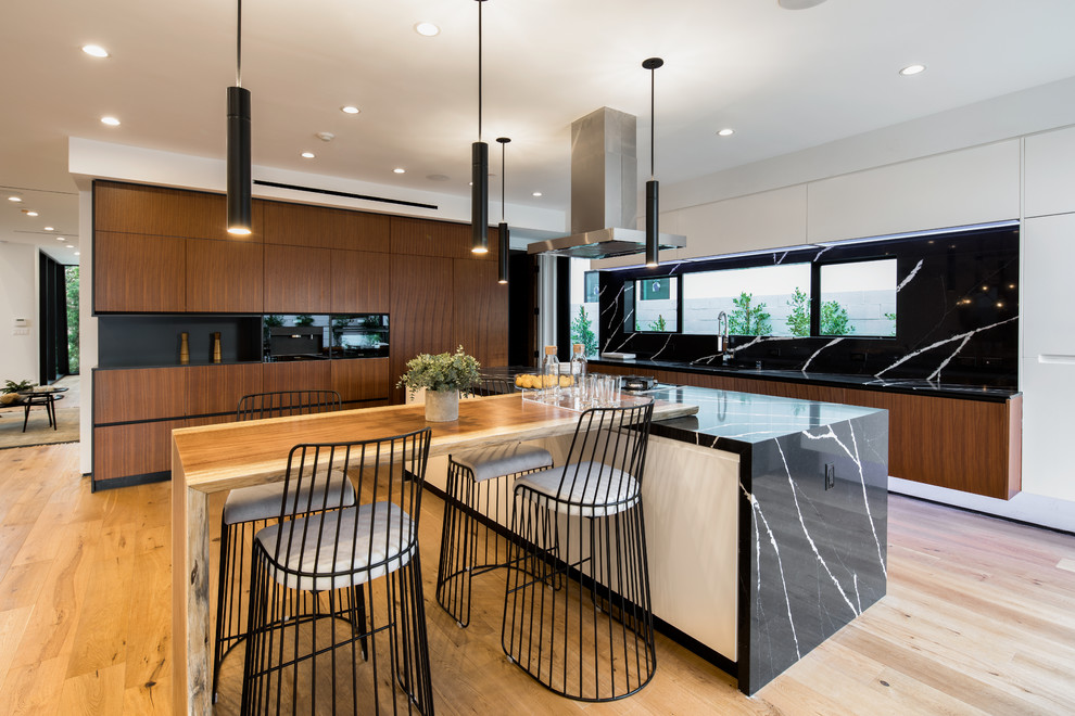 Photo of a large contemporary l-shaped open plan kitchen in Los Angeles with medium wood cabinets, granite benchtops, black splashback, light hardwood floors, with island, beige floor, flat-panel cabinets and black appliances.
