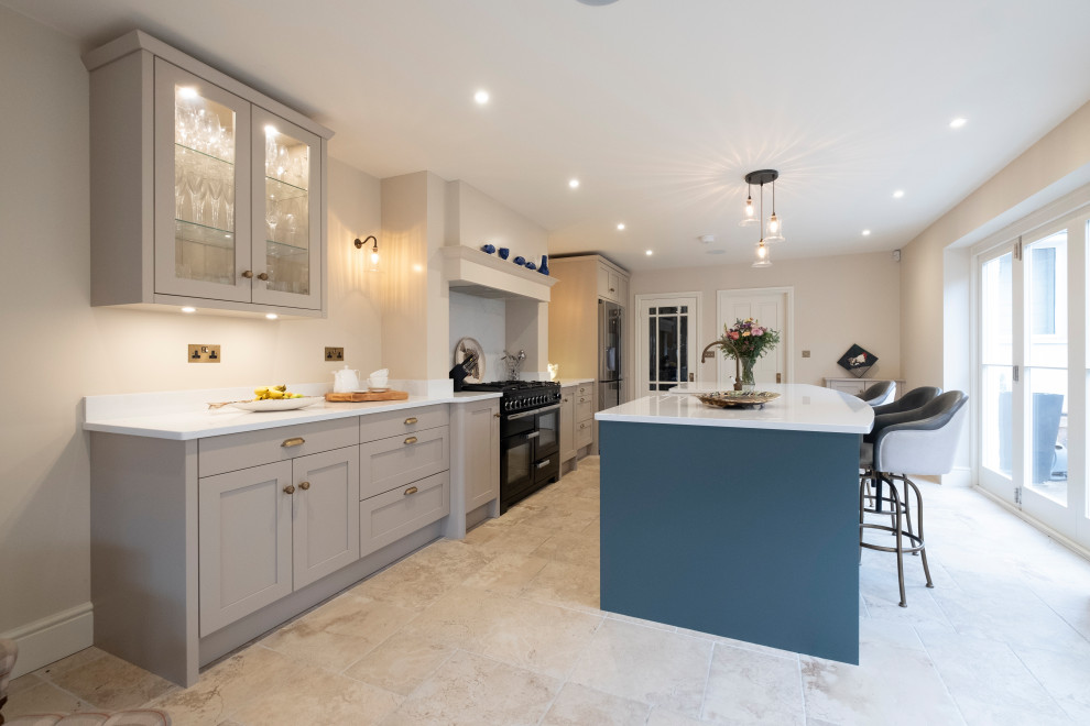 This is an example of a large traditional single-wall open plan kitchen in Cardiff with a belfast sink, shaker cabinets, quartz worktops, limestone flooring, an island, white worktops and a chimney breast.