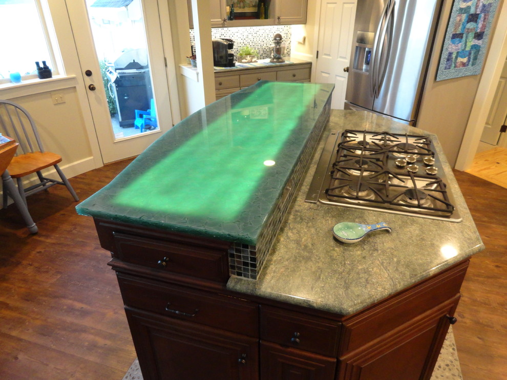 This is an example of a large beach style u-shaped eat-in kitchen in Seattle with raised-panel cabinets, dark wood cabinets, glass benchtops, green splashback, glass sheet splashback, stainless steel appliances, dark hardwood floors and with island.