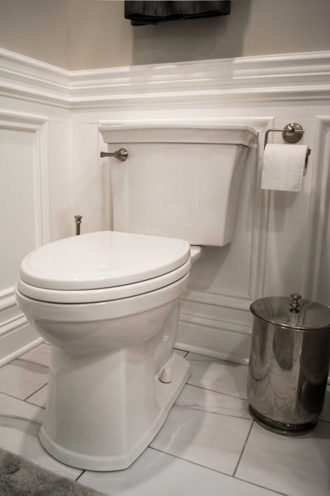 This is an example of a mid-sized transitional master bathroom in Louisville with raised-panel cabinets, brown cabinets, a corner shower, a one-piece toilet, white tile, ceramic tile, beige walls, marble floors, an undermount sink, engineered quartz benchtops, a hinged shower door and beige benchtops.