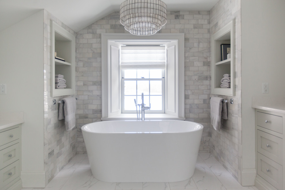 This is an example of a mid-sized contemporary master bathroom in Toronto with shaker cabinets, grey cabinets, a freestanding tub, white walls, marble floors, white floor, an alcove shower, a one-piece toilet, white tile, marble, an undermount sink, engineered quartz benchtops and a hinged shower door.