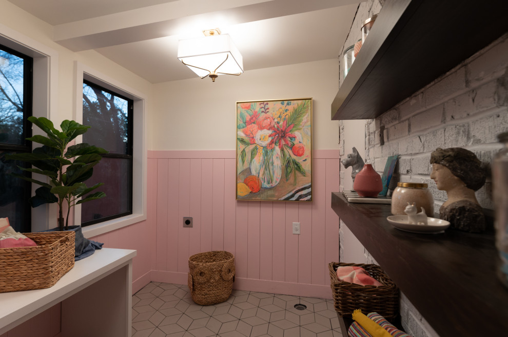 Foto på en tvättstuga, med vita skåp, vitt stänkskydd, stänkskydd i tegel, rosa väggar, klinkergolv i porslin och vitt golv