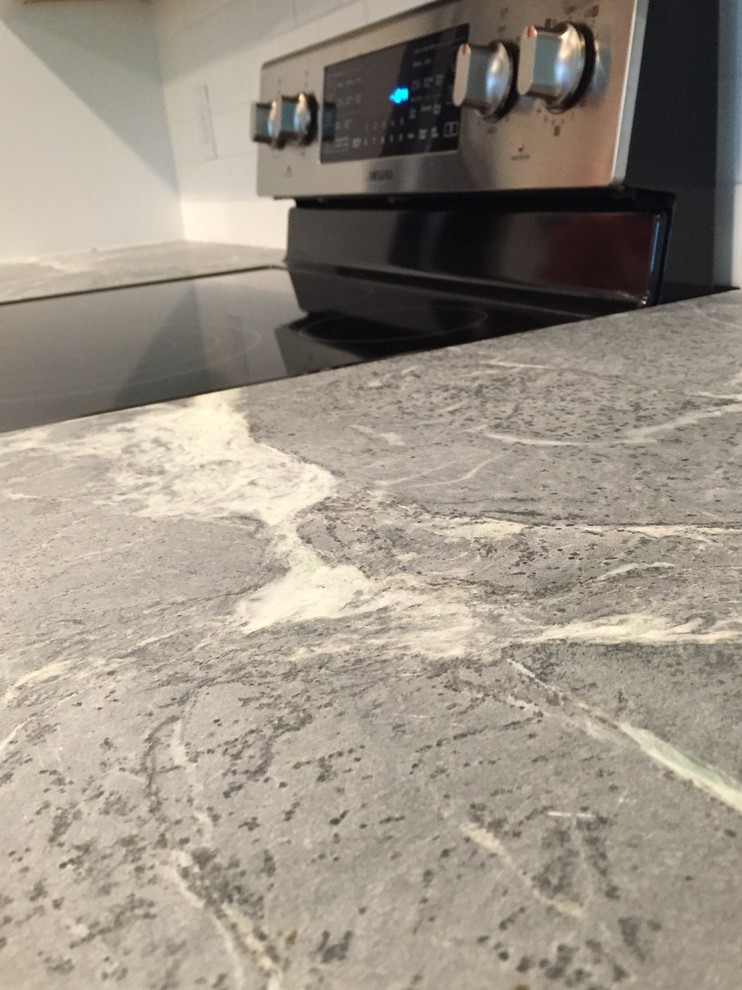 Mid-sized transitional l-shaped medium tone wood floor enclosed kitchen photo in Other with an undermount sink, shaker cabinets, white cabinets, soapstone countertops, white backsplash, subway tile backsplash, stainless steel appliances and a peninsula