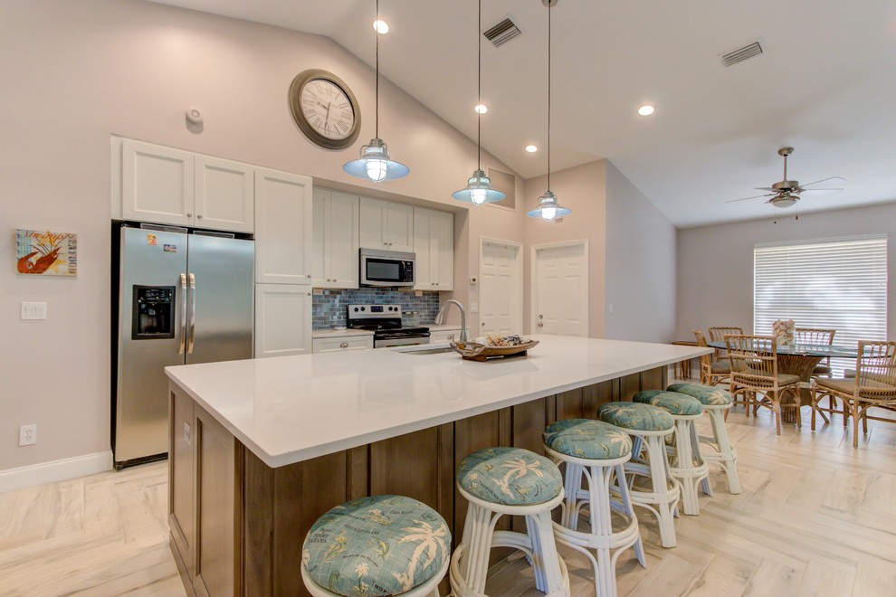 Large single-wall porcelain tile and white floor open concept kitchen photo with an undermount sink, shaker cabinets, white cabinets, quartz countertops, blue backsplash, stainless steel appliances, an island and white countertops