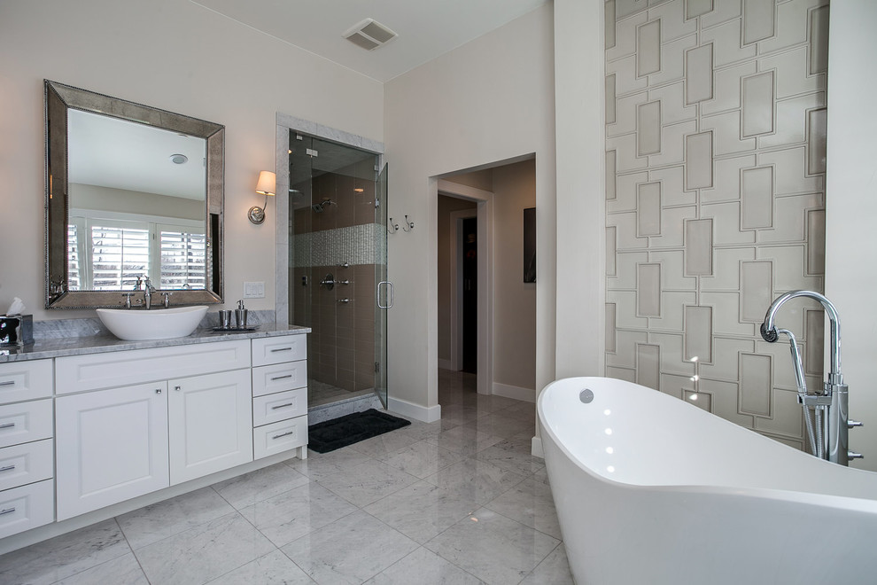 This is an example of a mid-sized contemporary master wet room bathroom in Denver with flat-panel cabinets, white cabinets, a freestanding tub, beige walls, marble floors, a vessel sink, granite benchtops and a hinged shower door.