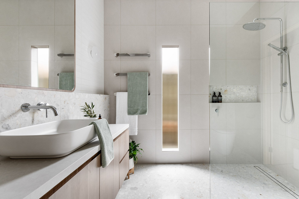 Modern inredning av ett mellanstort vit vitt en-suite badrum, med släta luckor, skåp i ljust trä, en öppen dusch, en vägghängd toalettstol, grå kakel, tunnelbanekakel, grå väggar, cementgolv, ett fristående handfat, bänkskiva i kalksten, grått golv och med dusch som är öppen