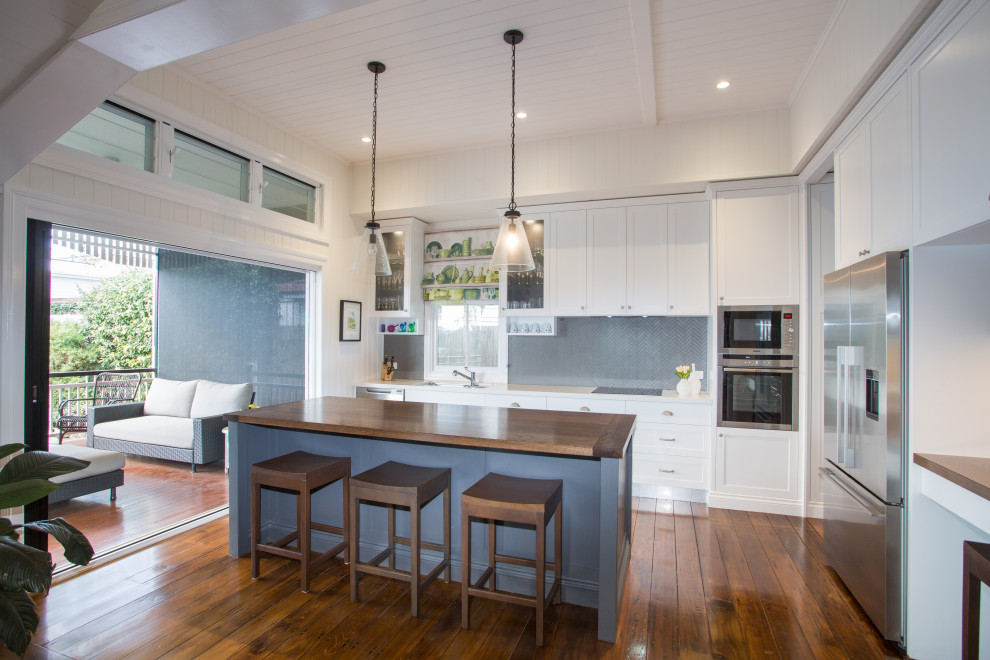 Photo of a transitional l-shaped kitchen in Brisbane with shaker cabinets, white cabinets, grey splashback, mosaic tile splashback, stainless steel appliances, dark hardwood floors, with island, brown floor, white benchtop and timber.