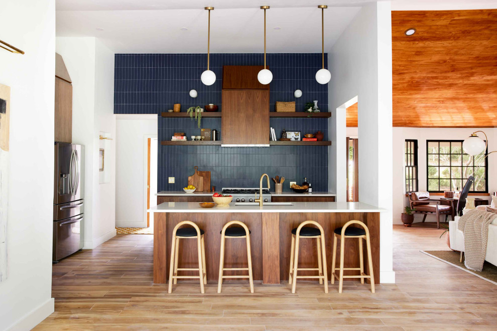 Inspiration for a mid-sized midcentury galley open plan kitchen in Oklahoma City with an undermount sink, flat-panel cabinets, brown cabinets, quartz benchtops, blue splashback, ceramic splashback, stainless steel appliances, with island, brown floor, white benchtop and vaulted.