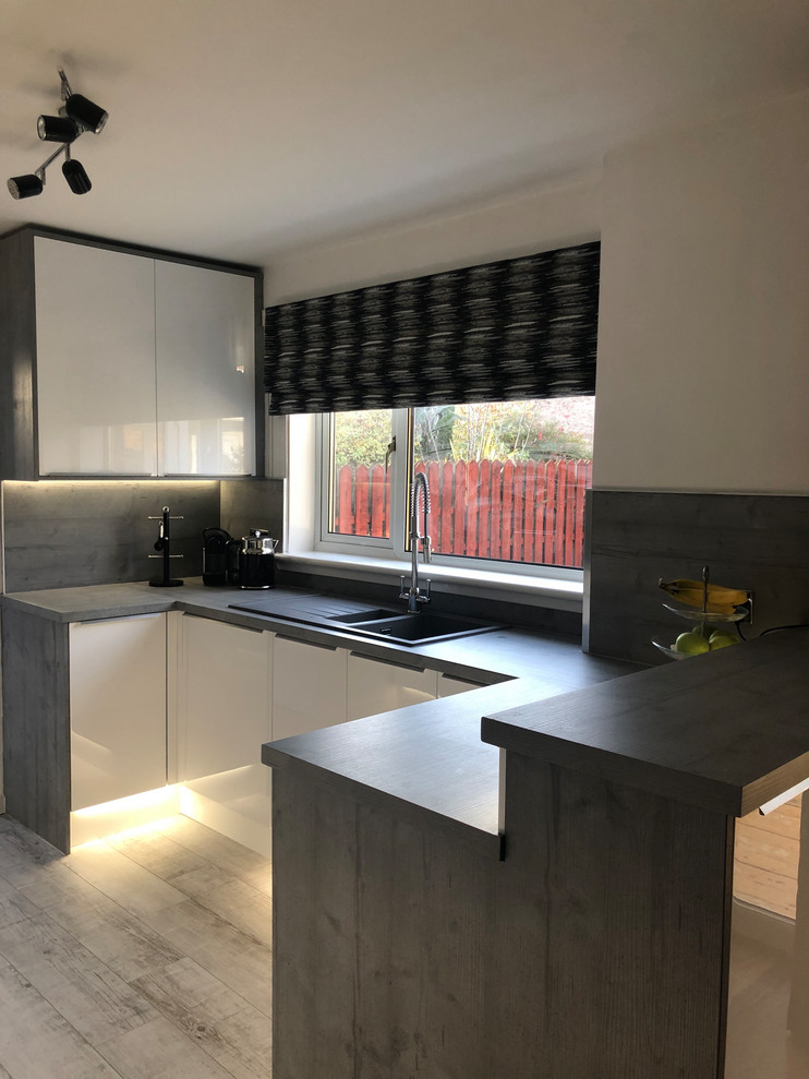 Mid-sized contemporary eat-in kitchen in Glasgow with an integrated sink, flat-panel cabinets, white cabinets, laminate benchtops, grey splashback, timber splashback, stainless steel appliances, vinyl floors, no island, grey floor and grey benchtop.