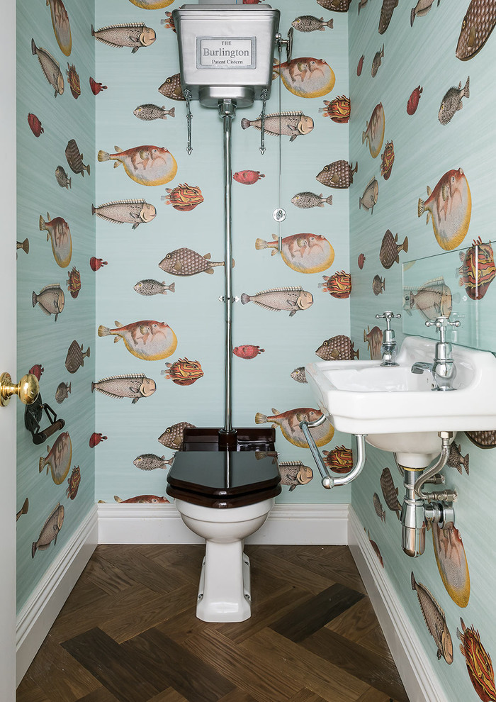 This is an example of a beach style powder room in London with a two-piece toilet, multi-coloured walls, dark hardwood floors and a wall-mount sink.