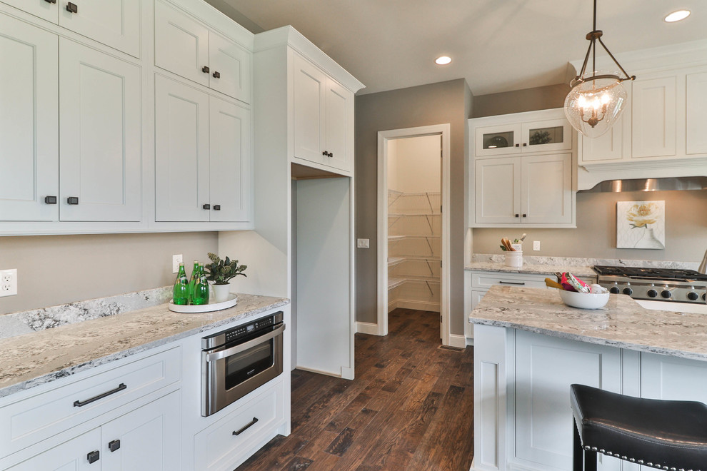 Inspiration for a mid-sized transitional l-shaped dark wood floor and brown floor open concept kitchen remodel in St Louis with a farmhouse sink, shaker cabinets, white cabinets, granite countertops, gray backsplash, stainless steel appliances and an island