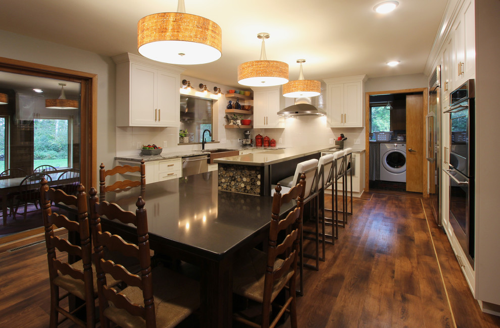 Open concept kitchen - mid-sized transitional l-shaped open concept kitchen idea with a farmhouse sink, beaded inset cabinets, white cabinets, quartzite countertops, white backsplash, stainless steel appliances and an island
