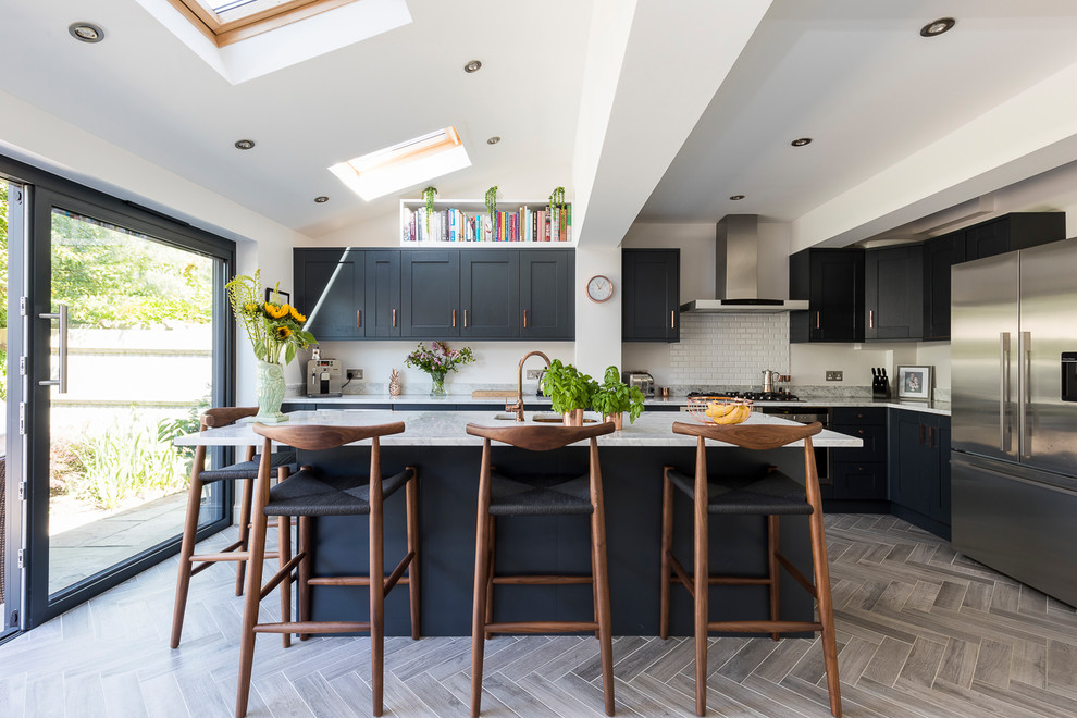 Mid-sized contemporary l-shaped kitchen in London with recessed-panel cabinets, blue cabinets, marble benchtops, white splashback, subway tile splashback, stainless steel appliances, a peninsula and grey floor.