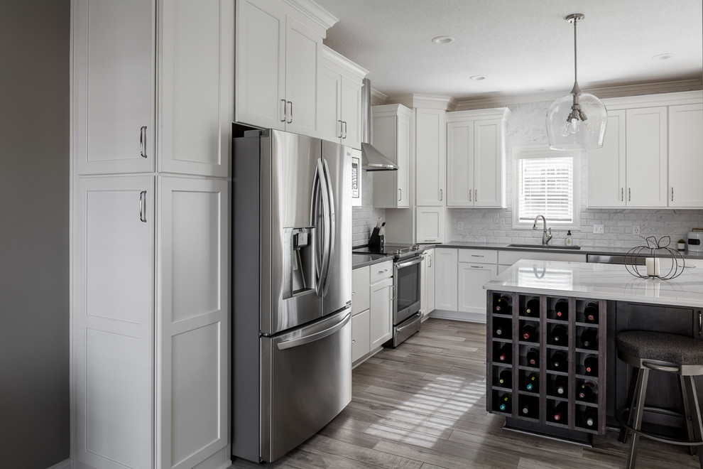 Example of a mid-sized transitional l-shaped ceramic tile and gray floor eat-in kitchen design with an undermount sink, shaker cabinets, white cabinets, quartz countertops, white backsplash, marble backsplash, stainless steel appliances, an island and gray countertops