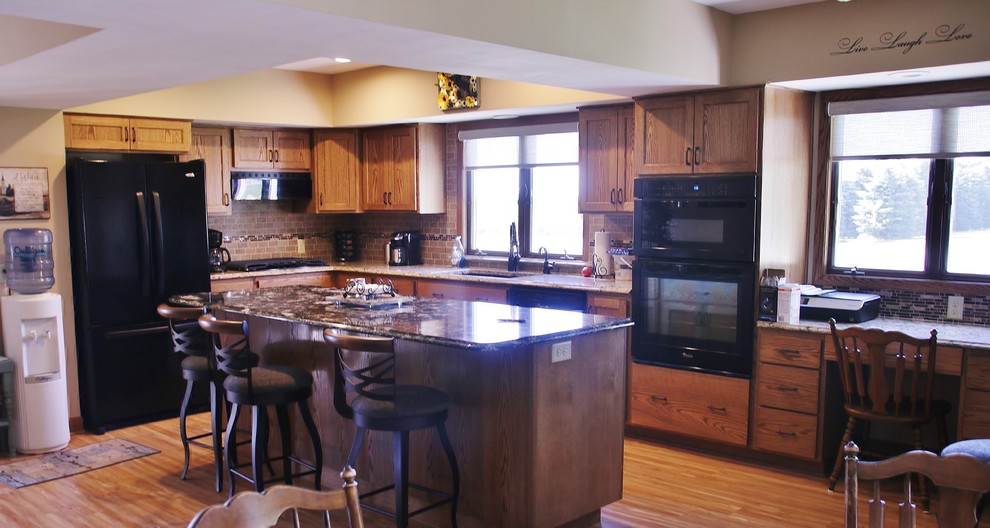 Mid-sized l-shaped eat-in kitchen photo with flat-panel cabinets, medium tone wood cabinets, quartz countertops, beige backsplash, black appliances and an island