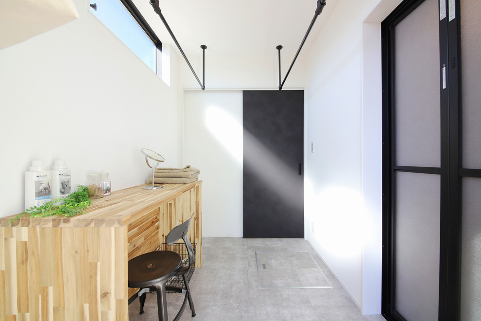 他の地域にあるインダストリアルスタイルのおしゃれな家事室 (白い壁、茶色いキッチンカウンター、セラミックタイルの床、グレーの床) の写真