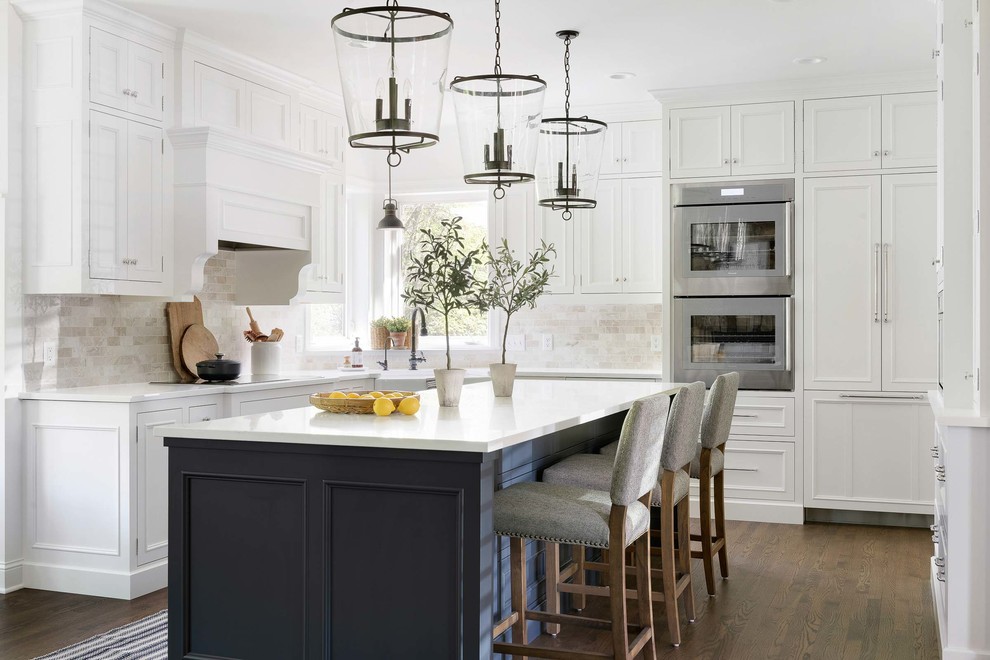 Inspiration for a traditional u-shaped eat-in kitchen in Minneapolis with a farmhouse sink, white cabinets, white splashback, dark hardwood floors, with island, brown floor, white benchtop, white appliances and recessed-panel cabinets.
