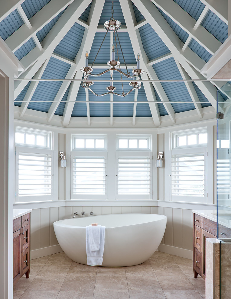This is an example of a beach style master bathroom in Raleigh with medium wood cabinets, a freestanding tub, beige walls, beige floor and recessed-panel cabinets.