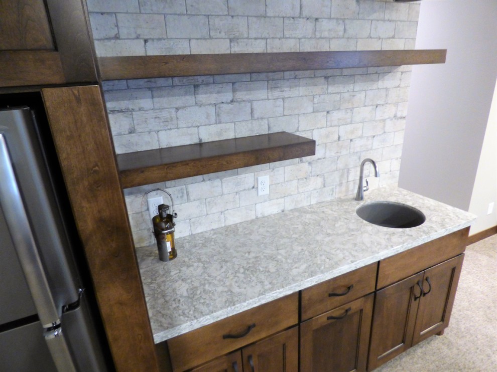 Small transitional single-wall wet bar in Other with an undermount sink, recessed-panel cabinets, brown cabinets, quartz benchtops, grey splashback, ceramic splashback, carpet and beige floor.