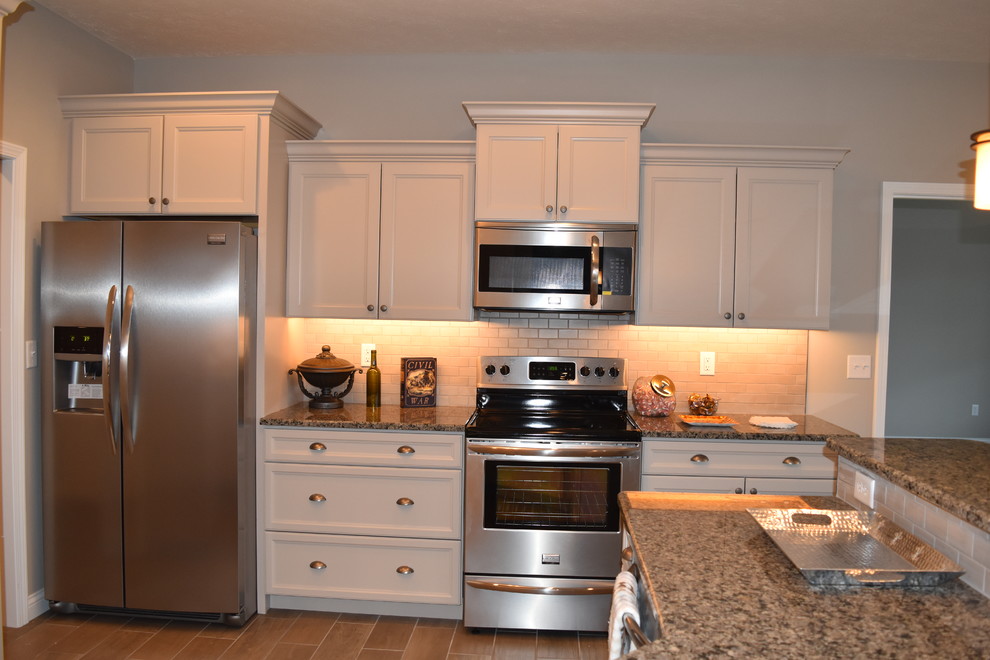 Example of a mid-sized transitional u-shaped porcelain tile enclosed kitchen design with an undermount sink, recessed-panel cabinets, beige cabinets, granite countertops, beige backsplash, subway tile backsplash, stainless steel appliances and a peninsula
