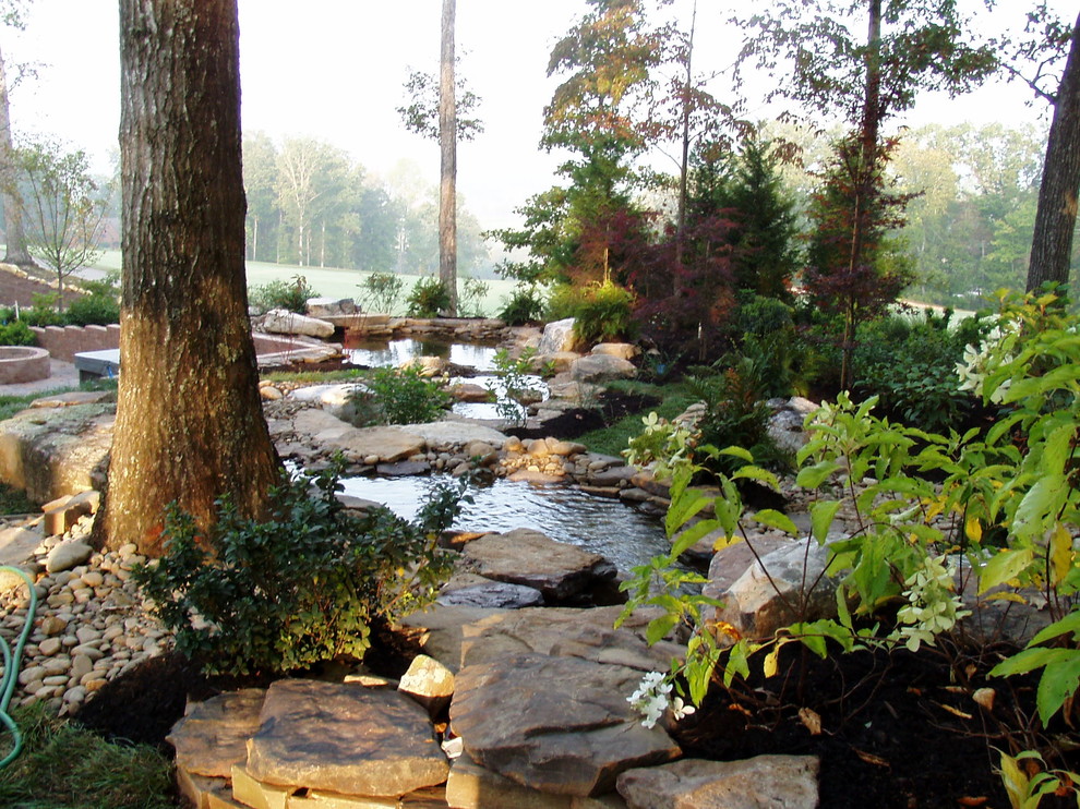 Large traditional backyard shaded formal garden in Other with natural stone pavers and with rock feature.