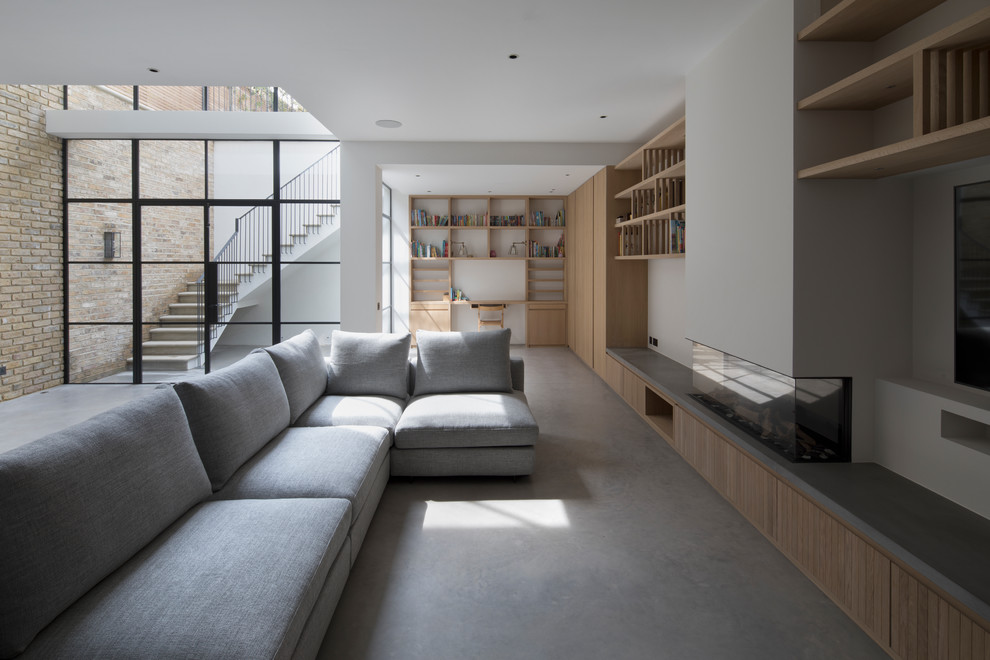 Inspiration for an expansive modern open concept family room in London with white walls, a ribbon fireplace, a plaster fireplace surround, concrete floors and grey floor.
