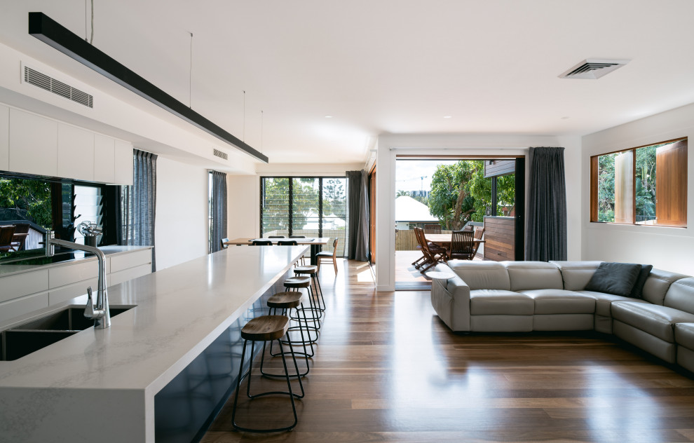 Photo of a mid-sized contemporary galley open plan kitchen in Brisbane with an undermount sink, flat-panel cabinets, white cabinets, quartz benchtops, white splashback, glass sheet splashback, black appliances, dark hardwood floors, with island, brown floor and white benchtop.