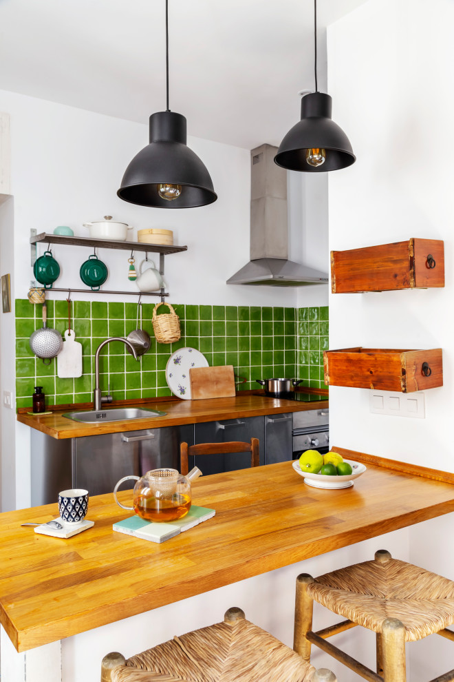 Photo of an eclectic galley kitchen in Madrid with a drop-in sink, flat-panel cabinets, stainless steel cabinets, wood benchtops, green splashback, stainless steel appliances, a peninsula and brown benchtop.