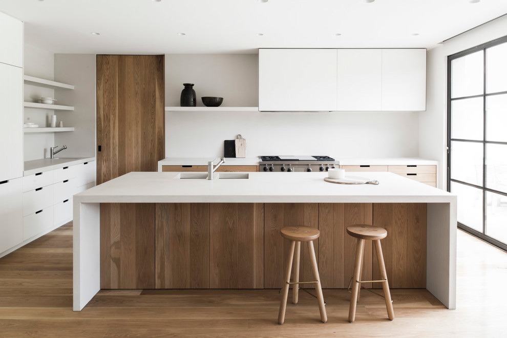 Inspiration for a contemporary u-shaped kitchen in Melbourne with an undermount sink, flat-panel cabinets, white cabinets, white splashback, medium hardwood floors, with island, brown floor and white benchtop.