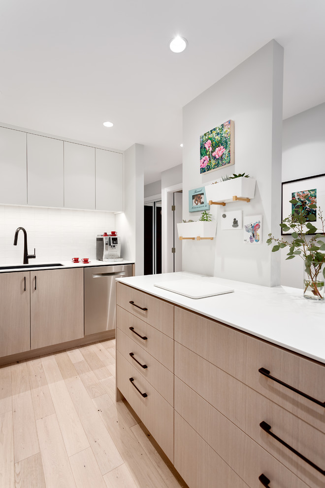 Design ideas for a small contemporary l-shaped eat-in kitchen in Vancouver with an undermount sink, flat-panel cabinets, light wood cabinets, solid surface benchtops, white splashback, subway tile splashback, stainless steel appliances, light hardwood floors, with island and beige floor.