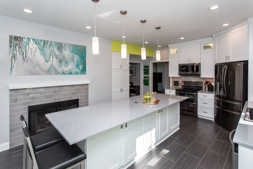 Example of a mid-sized transitional u-shaped porcelain tile enclosed kitchen design with a drop-in sink, recessed-panel cabinets, white cabinets, quartz countertops, gray backsplash, ceramic backsplash, stainless steel appliances and an island
