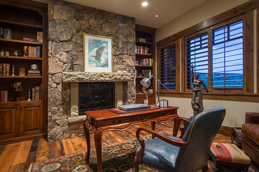 This is an example of a mid-sized country study room in Salt Lake City with white walls, medium hardwood floors, a standard fireplace, a stone fireplace surround and a freestanding desk.