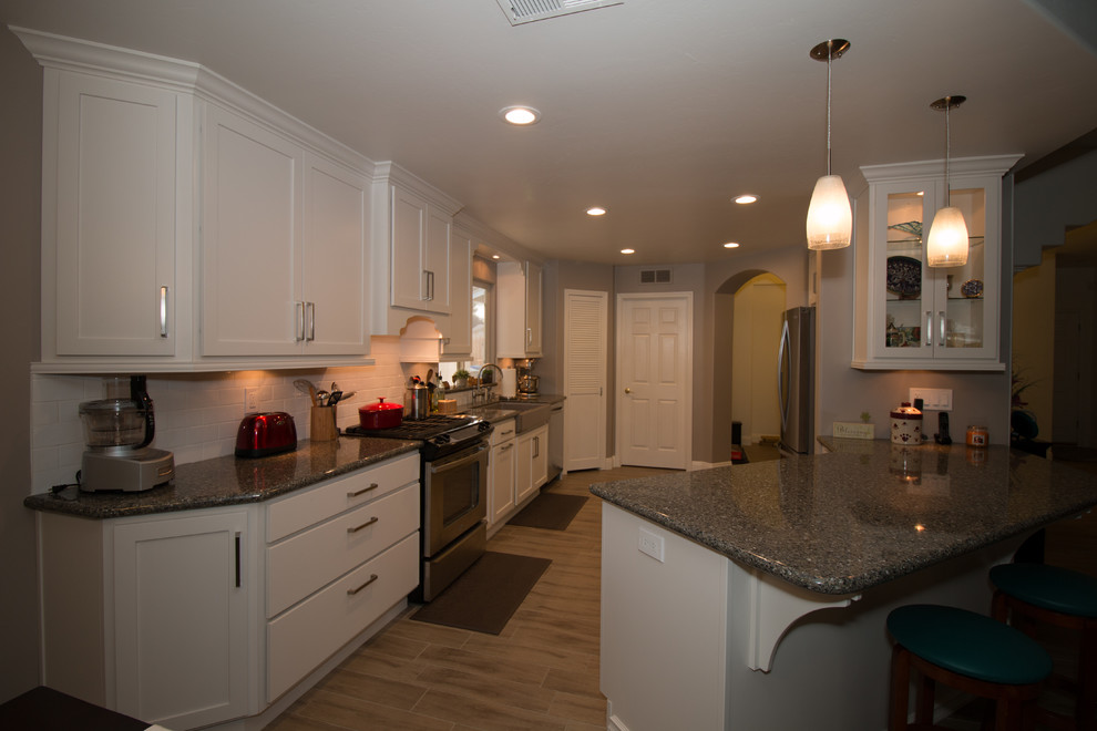 Example of a mid-sized transitional galley porcelain tile open concept kitchen design with a farmhouse sink, shaker cabinets, white cabinets, quartz countertops, white backsplash, subway tile backsplash and stainless steel appliances