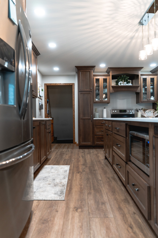 Huge transitional l-shaped medium tone wood floor and brown floor open concept kitchen photo with shaker cabinets, medium tone wood cabinets, quartz countertops, stainless steel appliances, an island and white countertops