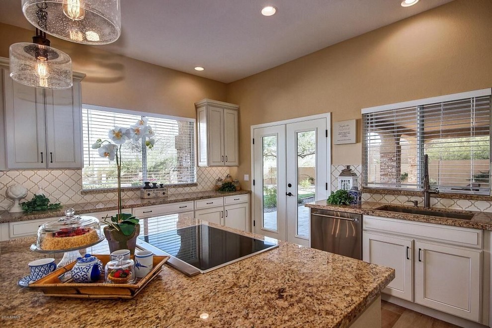 Inspiration for a large transitional medium tone wood floor and brown floor kitchen remodel in Phoenix with an undermount sink, beaded inset cabinets, white cabinets, granite countertops, white backsplash, ceramic backsplash, stainless steel appliances and an island