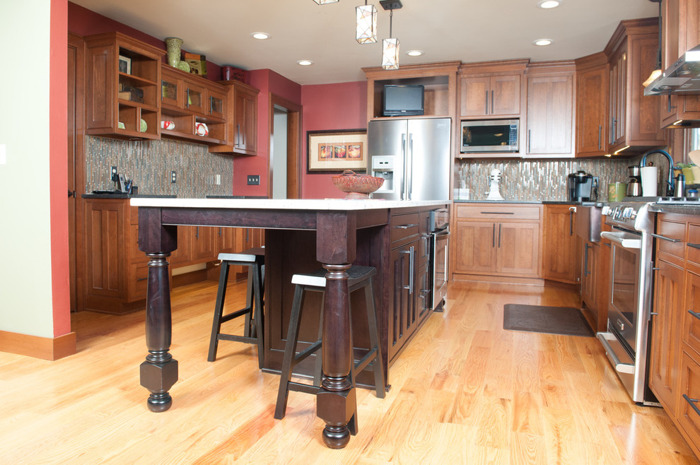 Example of a mid-sized transitional l-shaped medium tone wood floor eat-in kitchen design in Orange County with a farmhouse sink, shaker cabinets, medium tone wood cabinets, granite countertops, multicolored backsplash, matchstick tile backsplash, stainless steel appliances and an island