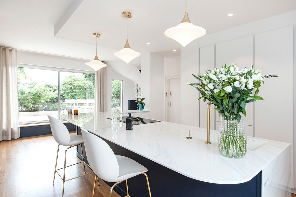 This is an example of a large contemporary galley eat-in kitchen in Paris with an integrated sink, flat-panel cabinets, white cabinets, with island, white benchtop, marble benchtops, panelled appliances, light hardwood floors and brown floor.