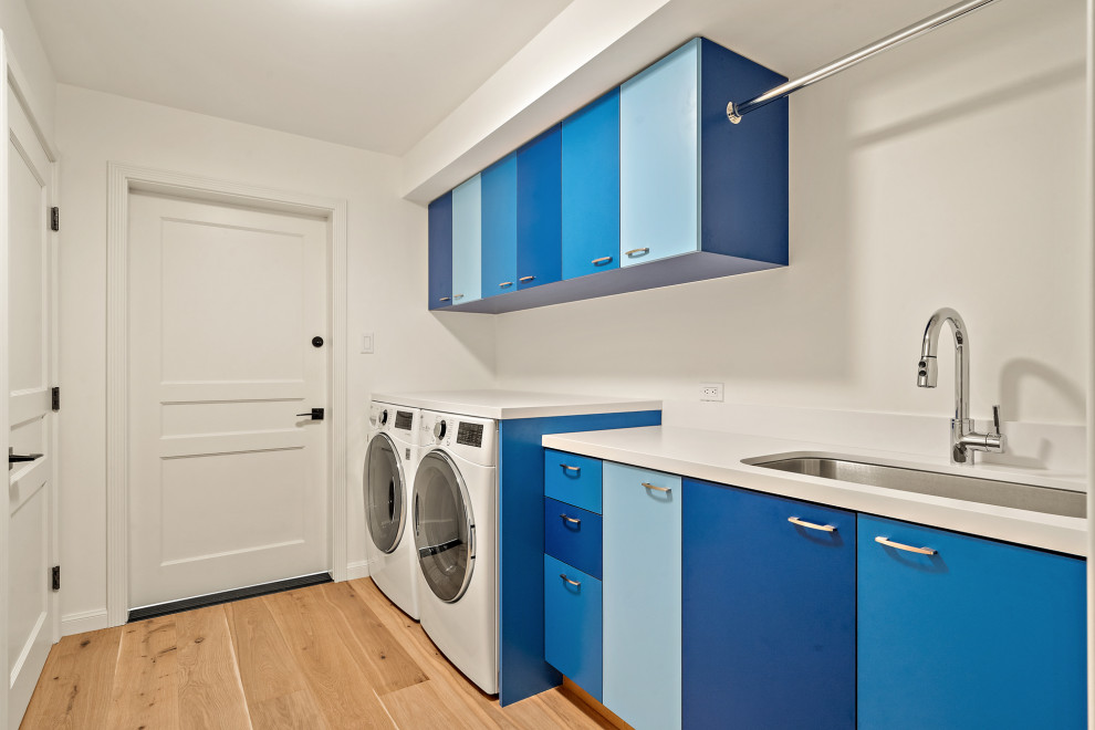Inspiration for a mid-sized midcentury single-wall dedicated laundry room in San Francisco with an undermount sink, flat-panel cabinets, blue cabinets, solid surface benchtops, white splashback, engineered quartz splashback, white walls, laminate floors, a side-by-side washer and dryer, brown floor and white benchtop.