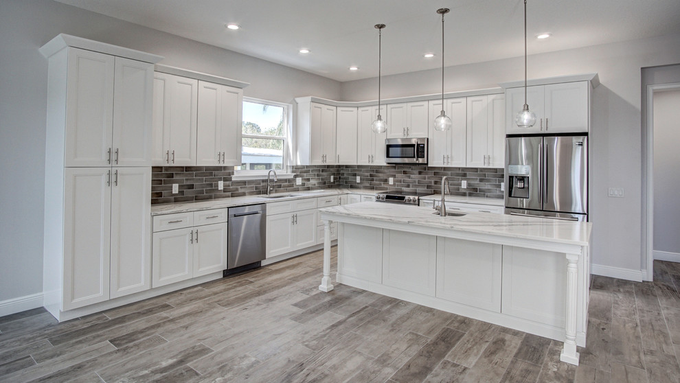 Large beach style l-shaped eat-in kitchen in Tampa with a single-bowl sink, recessed-panel cabinets, white cabinets, granite benchtops, grey splashback, porcelain splashback, stainless steel appliances, ceramic floors, with island, grey floor and white benchtop.