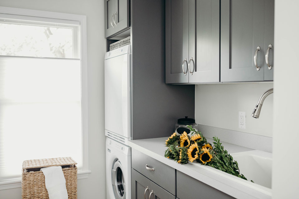 Inspiration for a large transitional single-wall dedicated laundry room in Detroit with an utility sink, shaker cabinets, white walls, a stacked washer and dryer, grey benchtop, grey cabinets, laminate benchtops, ceramic floors and grey floor.